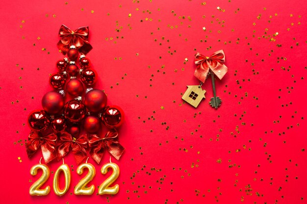 Christmas tree made of glass balls on red background with gold sequins and 2022 and House key. Christmas decor of finance, savings, loan in new year. Real estate, housing, mortgage, relocation