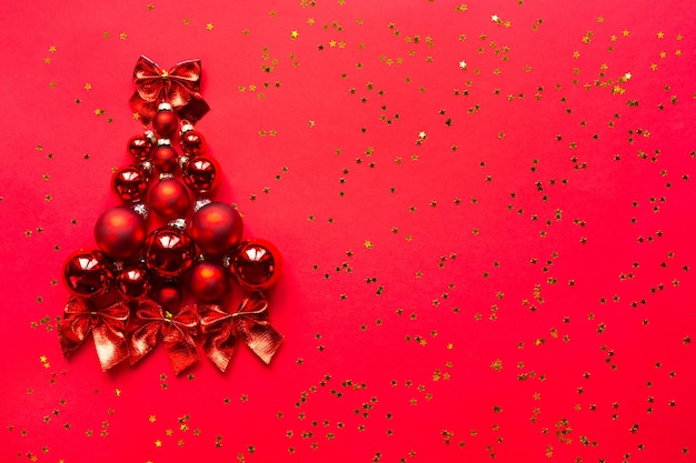 Christmas tree made of glass balls on a red background with gold stars. Christmas background, new year, flatlay. Copy space. Greeting card, festive mood