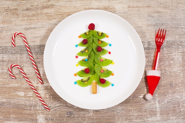 Albero di natale fatto di fette di kiwi sulla tavola di legno. idea creativa per la colazione di natale o per i dolci festivi di capodanno per bambini. vista dall'alto.