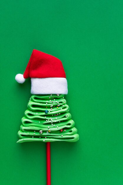 Christmas tree made of meringues in New Year's style on a green background. Christmas tree in a red santa hat.