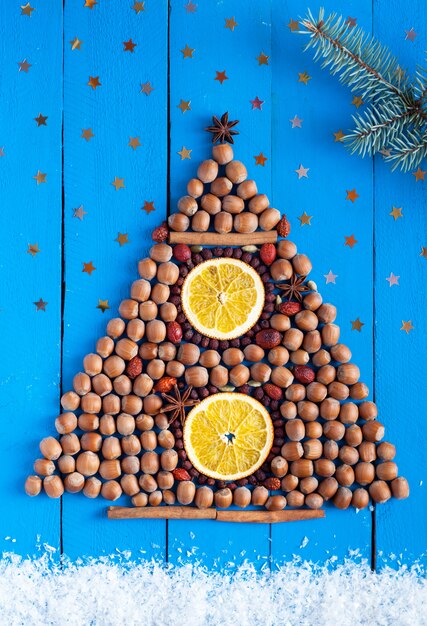 Christmas tree made of nuts and dried fruits on the wooden background with stars, snow and fir-tree branch