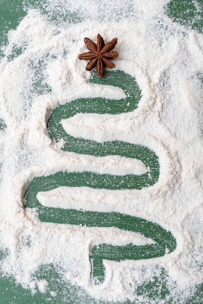 A Christmas tree painted from flour as from snow with a dried star of anise on a green background