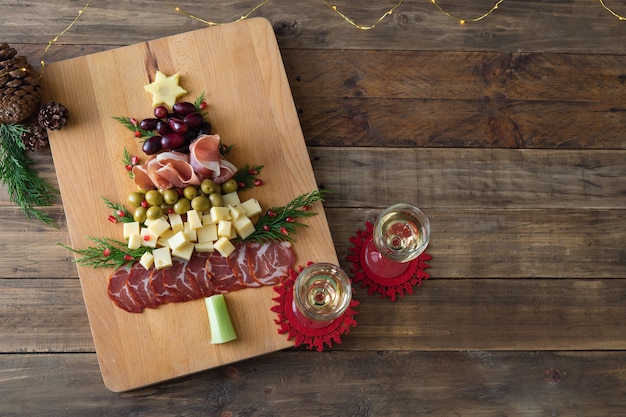 Christmas tree shaped cheese and charcuterie board with wooden background. Top view. Copy space.