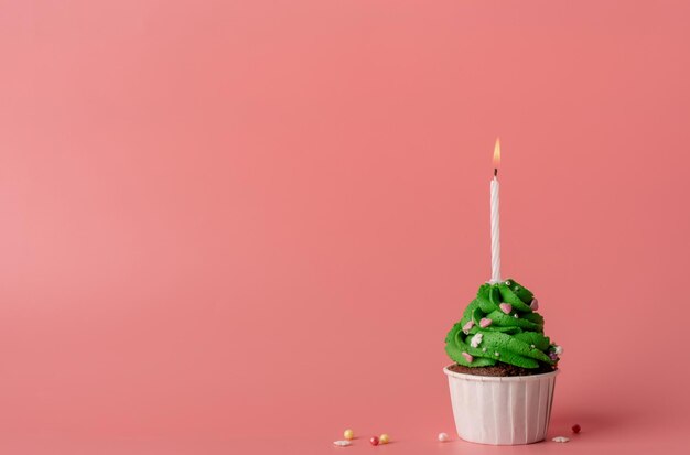 Christmas tree shaped cupcake with a candle on pink background