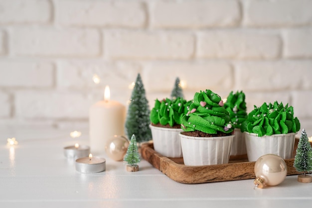 Christmas tree shaped cupcakes, surrounded with festive decorations and lights on the background