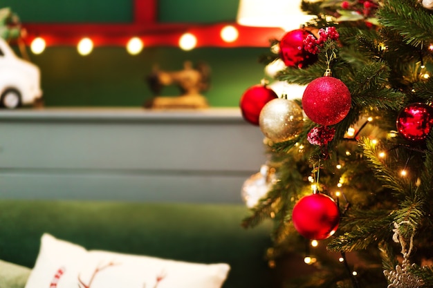 Christmas tree with red balls and a garland in a cozy room and a retro toys in the green wood background with garland.