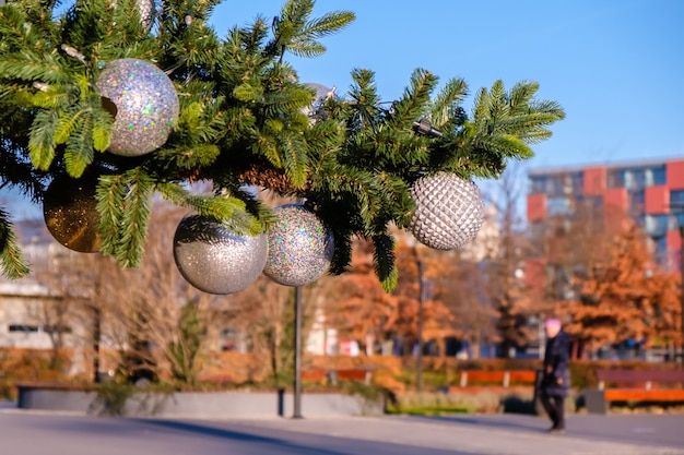 Рождественская елка с белыми елочными шарами на городской улице в солнечный летний день Размытая женщина гуляет