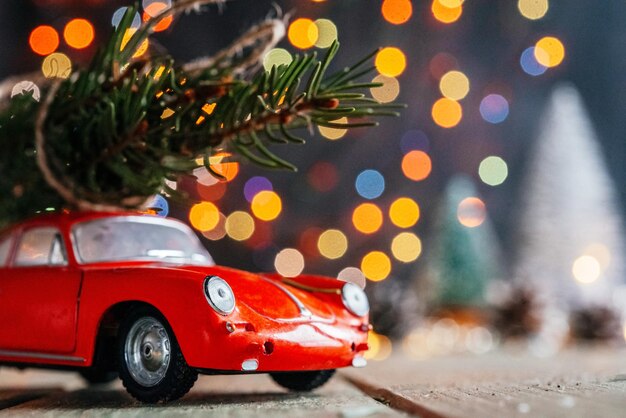 Foto argomento di consegna degli alberi di natale auto giocattolo rossa con albero di abete contro luci di natale colorate