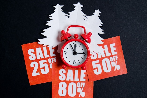 Photo christmas trees made of white paper on red stickers with discounts and a vintage clock