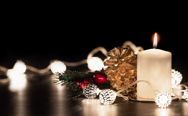 Christmas white candle with golden pine cone,mistletoe and light string glowing