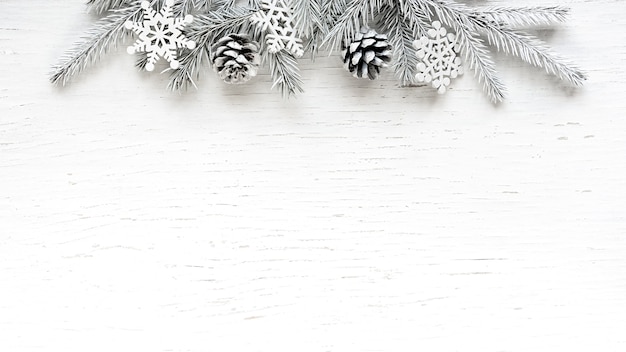 Christmas white Fir tree branches pine cones and snowflakes on white wooden background. Winter background with Copy space.