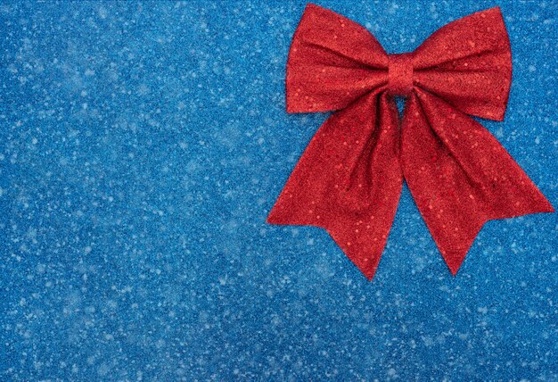 Christmas or winter blue background with red bow and snow. Xmas , winter concept. Flat lay style with copy space.