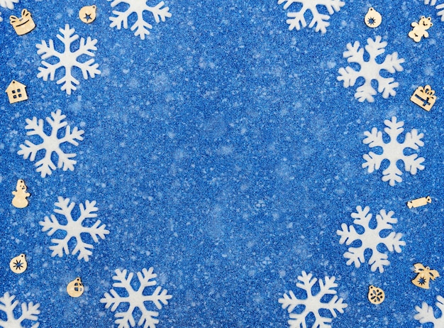 Christmas or winter blue background with white snowflakes, Xmas wooden decorations and snow. Flat lay style with copy space.