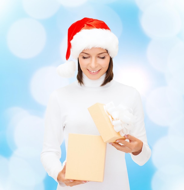 christmas, winter, happiness, holidays and people concept - smiling woman in santa helper hat opening gift box over blue lights background