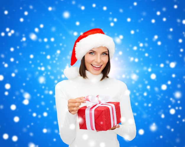 christmas, winter, happiness, holidays and people concept - smiling woman in santa helper hat with gift box over blue snowy background