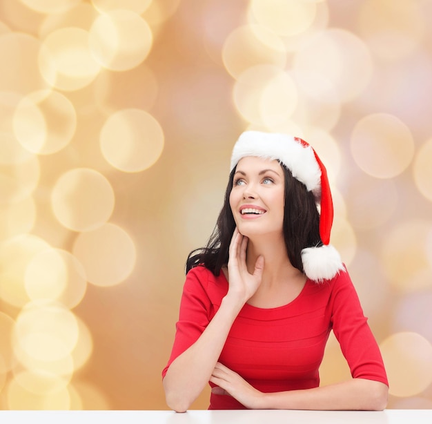christmas, winter, holidays, happiness and people concept - smiling woman in santa helper hat over beige lights background