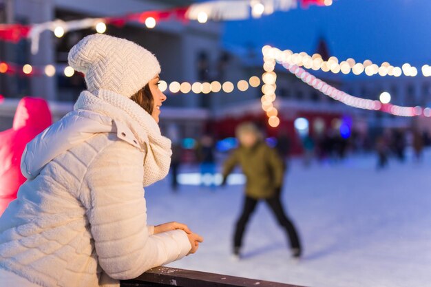 クリスマス、冬、レジャーのコンセプト-屋外のアイススケートリンクの近くの幸せな若い女性。