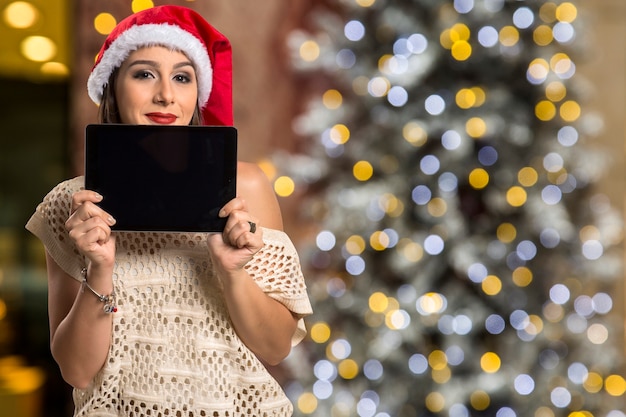 Foto compressa della holding del ritratto della donna di natale. donna felice sorridente sopra le luci del bokeh di natale