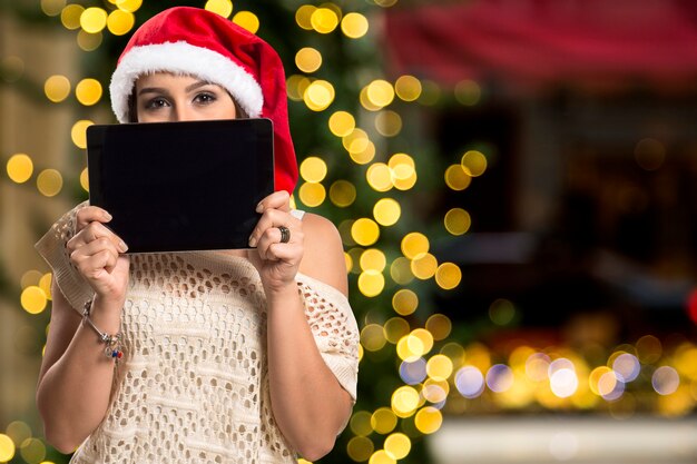 写真 タブレットを保持しているクリスマスの女性の肖像画。クリスマスのボケ味のライトで幸せな女性の笑顔