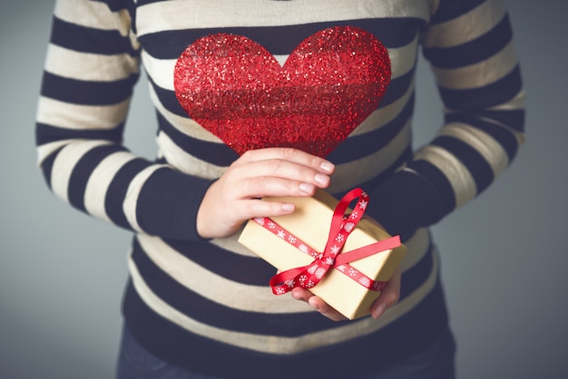 圣诞节的照片。一个穿着条纹毛衣，胸前有颗红心的女人。手里拿着圣诞礼物的女人。