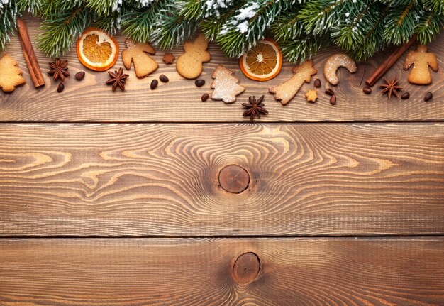 Christmas wooden background with snow fir tree spices and gingerbread cookies