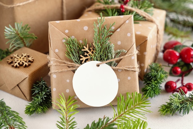 Regalo di natale avvolto con etichetta regalo di carta rotonda su un tavolo bianco con rami di abete e decorazioni da vicino. composizione invernale rustica con etichetta regalo vuota mockup, copia spazio