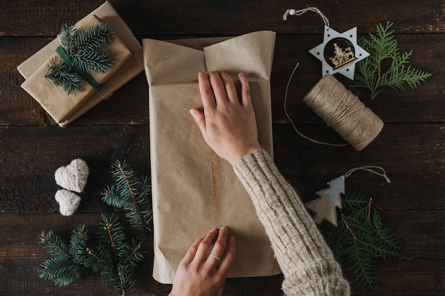 Идея рождественской упаковки рождественская упаковка рабочее пространство женские руки упаковывают подарочную коробку в переработанную крафт-бумагу