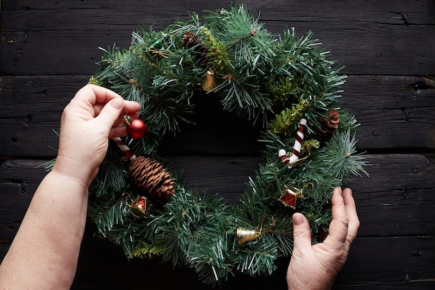 Christmas wreath on black wooden background with grandma hands decorating