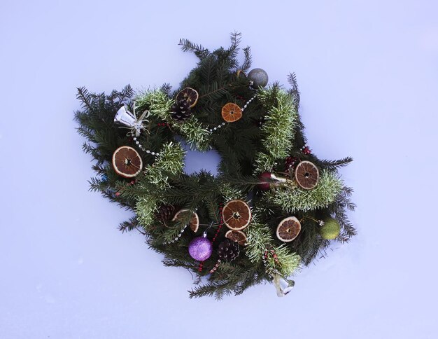 白い雪の背景にドライオレンジスライスとカラフルなボールで飾られたクリスマスリース。