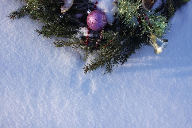 Рождественский венок украшен сухими дольками апельсина и красочными шарами на фоне белого снега.