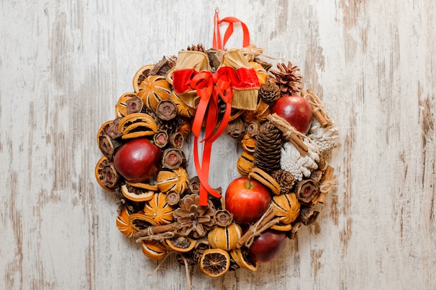 Corona di natale decorata con mele rosse, fette d'arancia essiccate, coni, bastoncini di cannella e fiocco