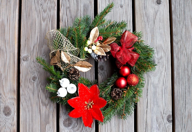 Christmas wreath decorated with red balls, lights and pinecones on a wood background