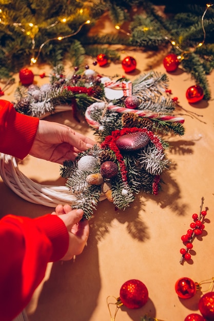 クリスマスリース、女性の手のクローズアップはトウヒの花輪を作り、赤いボールで飾る、