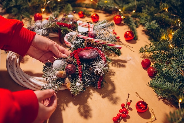 クリスマスリース、女性の手のクローズアップはトウヒの花輪を作り、赤いボールで飾る、