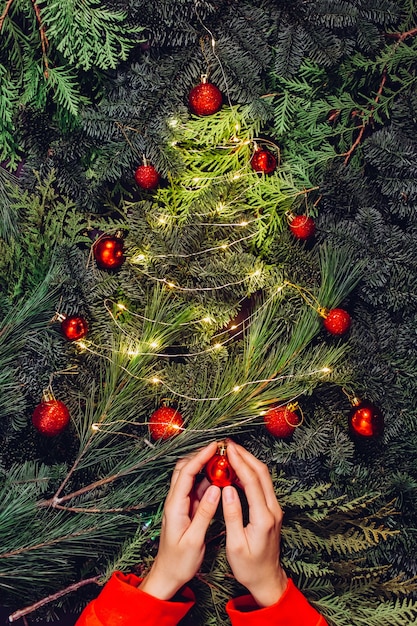 クリスマスリース、女性の手のクローズアップはトウヒの花輪を作り、赤いボールで飾る、