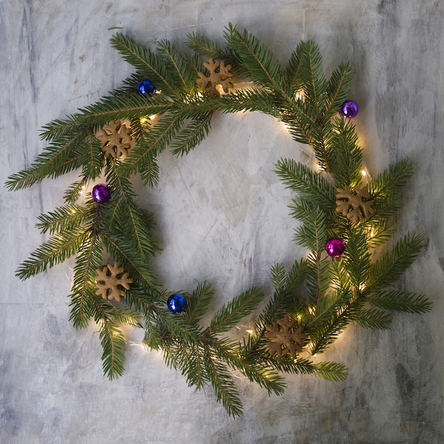 Corona di natale fatta di rami di abete, biscotti, palline colorate e luci incandescenti.