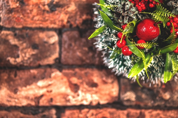 Christmas wreath of spruce and apples on a red brick wall.