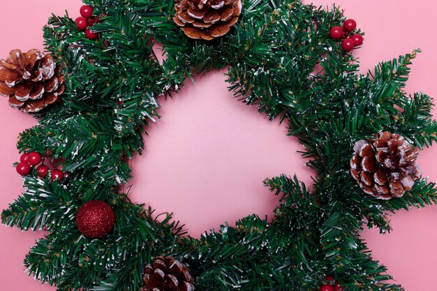 Photo christmas wreath with red balls berries and pine cones on a pink background copy space