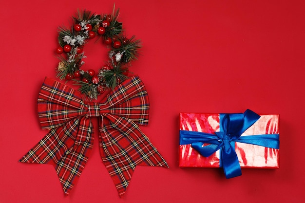 Christmas wreath with red bow, Christmas decorations and small gift on red background. Flat lay, top view, copy space. Minimalistic stylish background for design free space.