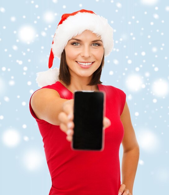 christmas, x-mas, electronics, gadget concept - smiling woman in santa helper hat with blank screen smartphone