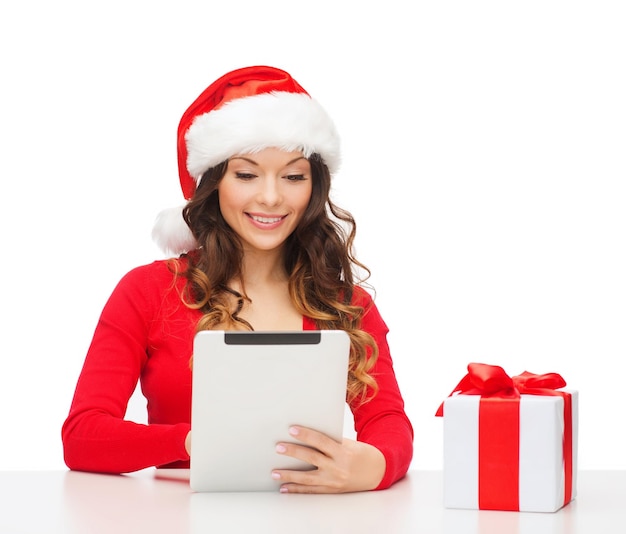 christmas, x-mas, online shopping concept - woman in santa helper hat with gift box and tablet pc computer