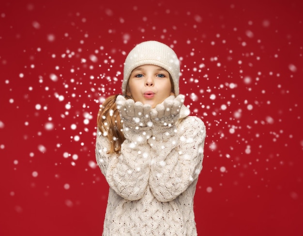 Foto natale, natale, persone, concetto di felicità - ragazza felice in abiti invernali che soffia sui palmi