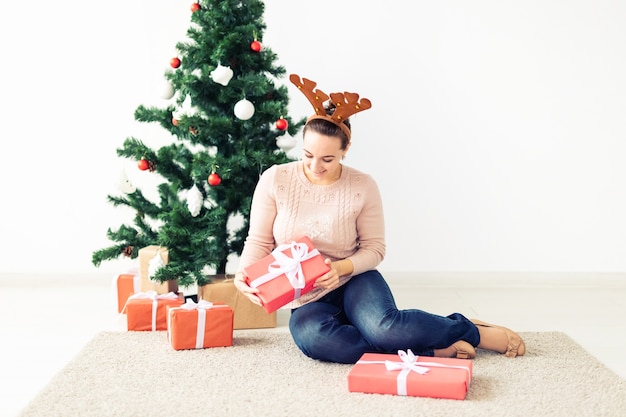Рождество, рождество, зима, концепция счастья - девушка открывает подарок на фоне елки. Счастливая молодая женщина празднует Рождество