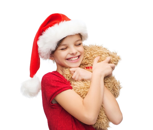 рождество, рождество, зима, концепция счастья - улыбающаяся девушка в шляпе санта-помощника с плюшевым мишкой
