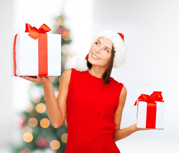 christmas, x-mas, winter, happiness concept - smiling woman in santa helper hat with many gift boxes