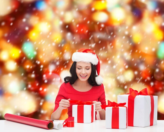 christmas, x-mas, winter, happiness concept - smiling woman in santa helper hat with many gift boxes