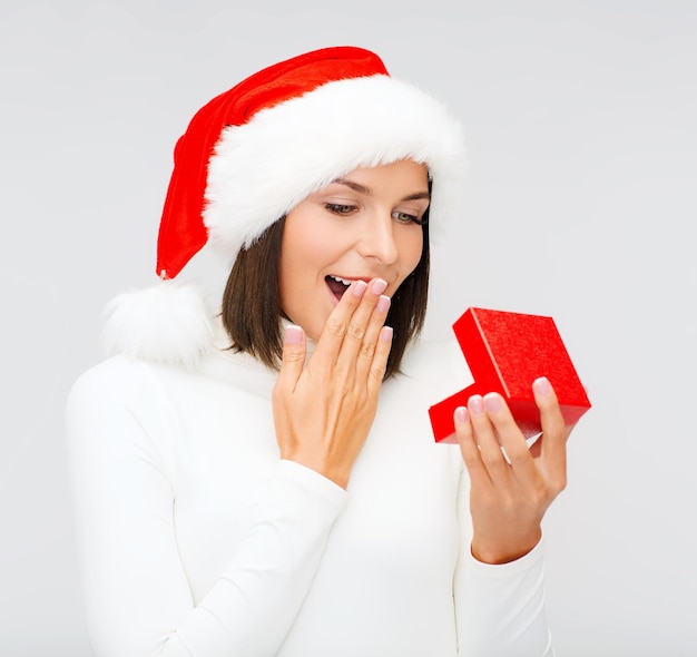 christmas, x-mas, winter, happiness concept - surprised woman in santa helper hat with small gift box