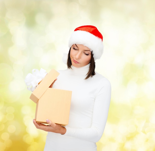 рождество, рождество, зима, концепция счастья - подозрительная женщина в шляпе Санта-помощника с подарочной коробкой