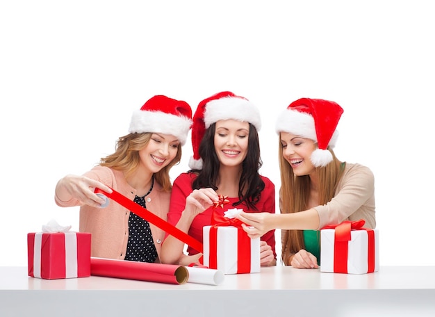 рождество, рождество, зима, концепция счастья - три улыбающиеся женщины в шляпах санта-помощника с подарочными коробками