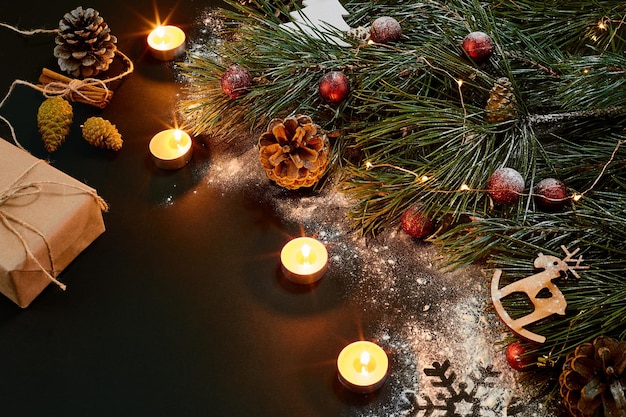 Christmas. Xmas toys, burning candles and spruce branch on black background top view. Copy space. Still life. Flat lay. New year